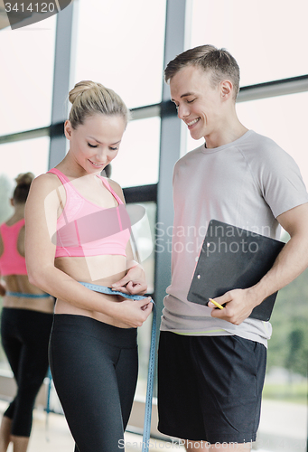 Image of smiling young woman with personal trainer in gym