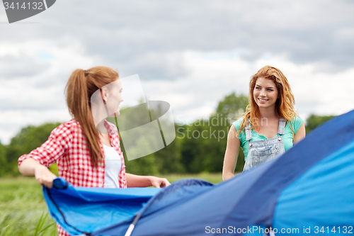 Image of smiling friends setting up tent outdoors