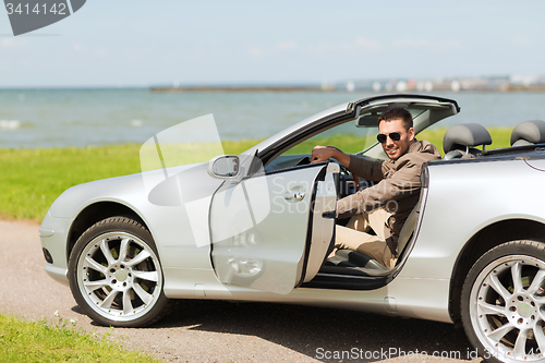 Image of happy man opening door of cabriolet car outdoors