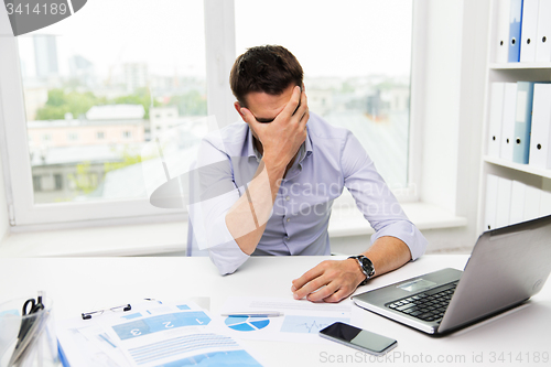 Image of businessman with laptop and papers in office