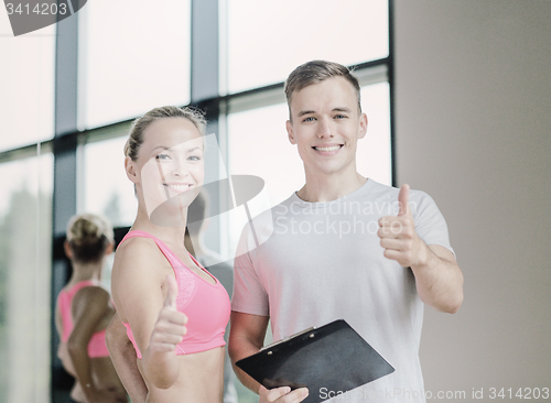 Image of smiling young woman with personal trainer in gym