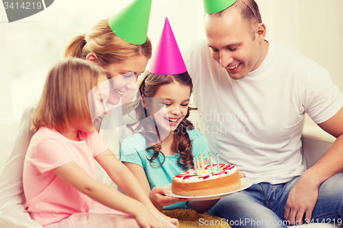 Image of smiling family with two kids in hats with cake