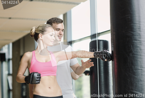 Image of smiling woman with personal trainer boxing in gym