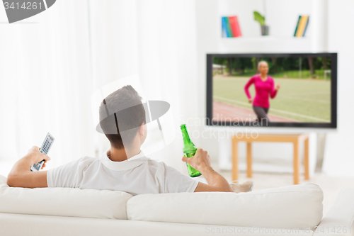 Image of man watching sport on tv and drinking beer at home