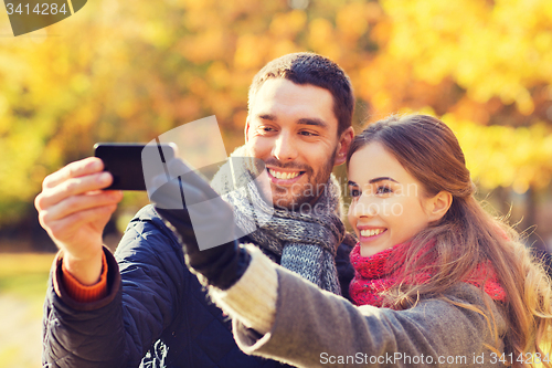Image of smiling couple with smartphone in autumn park