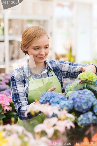 Image of happy woman taking care of flowers in greenhouse