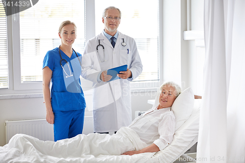 Image of doctor and nurse visiting senior woman at hospital