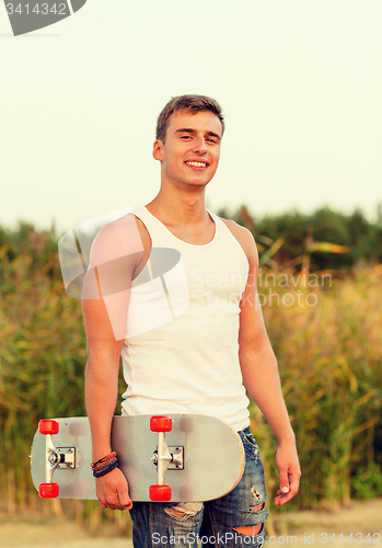 Image of smiling teenage boy with skateboard outdoors