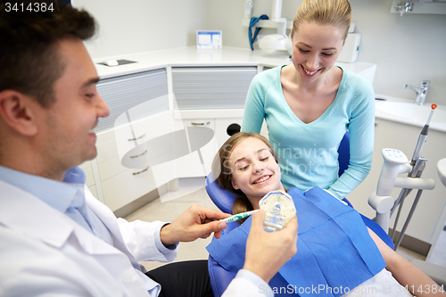 Image of happy dentist showing toothbrush to patient girl