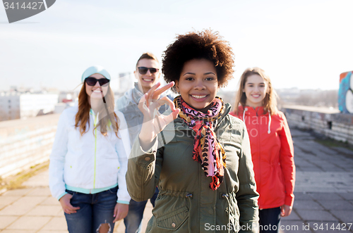 Image of happy teenage friends showing ok sign on street