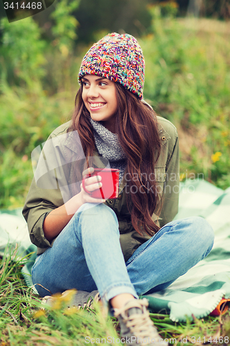 Image of smiling young woman with cup sitting in camping