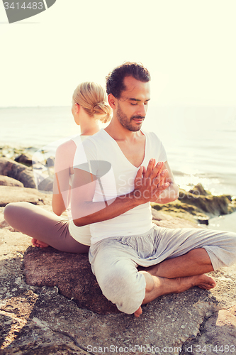 Image of smiling couple making yoga exercises outdoors