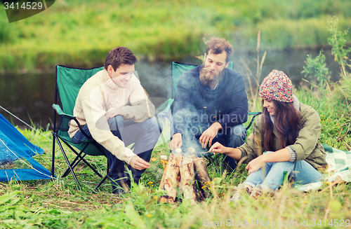 Image of smiling tourists cooking marshmallow in camping