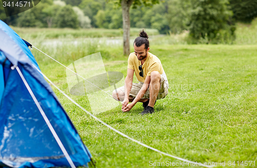 Image of happy man setting up tent outdoors