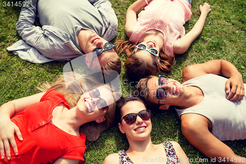 Image of group of smiling friends lying on grass outdoors