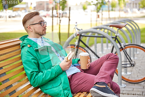 Image of happy young hipster man with coffee and sandwich