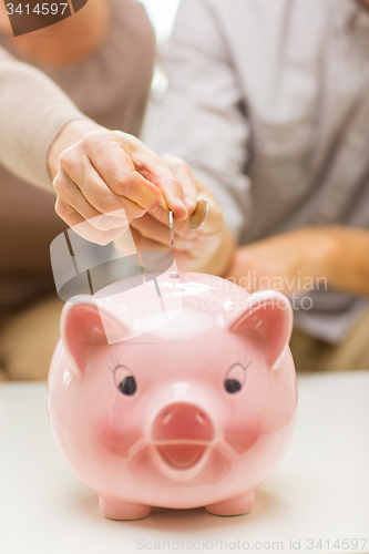 Image of close up of hands putting coin money to piggy bank