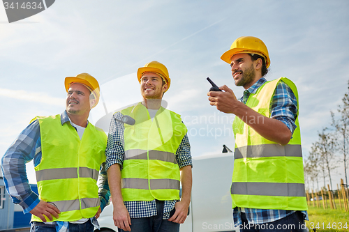 Image of happy male builders in vests with walkie talkie