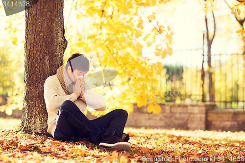 Image of ill man with paper tissue in autumn park