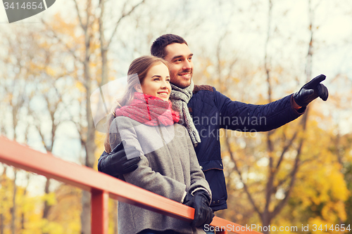 Image of smiling couple hugging on bridge in autumn park