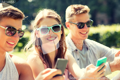 Image of smiling friends with smartphones sitting in park