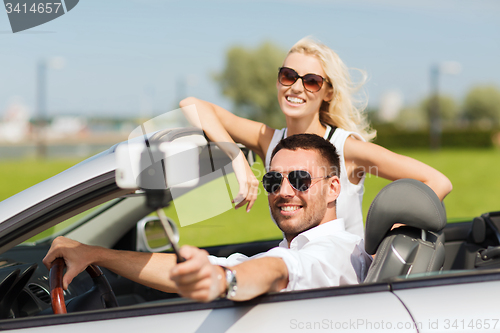 Image of happy couple in car taking selfie with smartphone