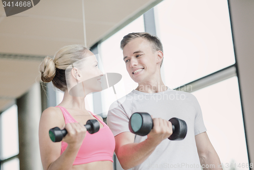 Image of smiling young woman with personal trainer in gym