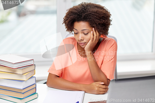 Image of bored african american woman doing homework home