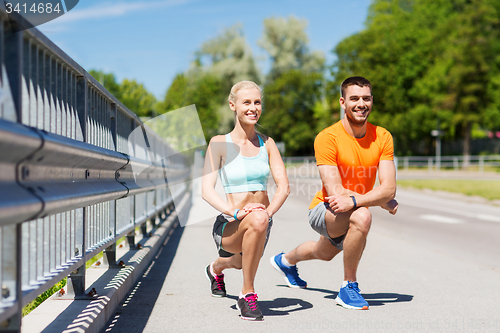 Image of smiling couple stretching leg outdoors