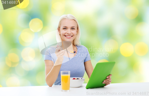 Image of smiling woman with tablet pc eating breakfast