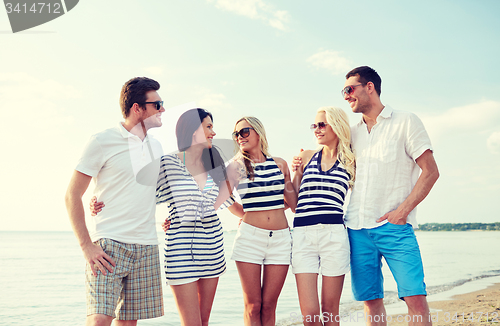 Image of smiling friends in sunglasses talking on beach
