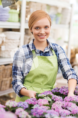 Image of happy woman taking care of flowers in greenhouse