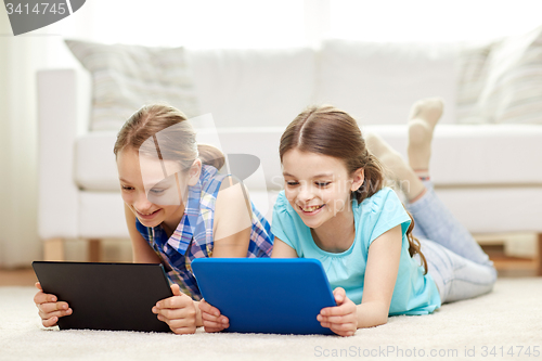 Image of happy girls with tablet pc lying on floor at home