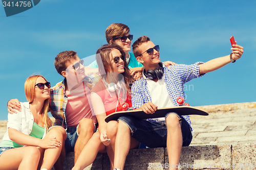 Image of group of smiling friends with smartphone outdoors