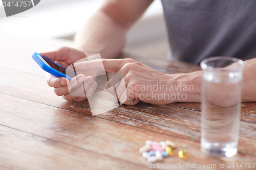 Image of close up of hands with smartphone, pills and water