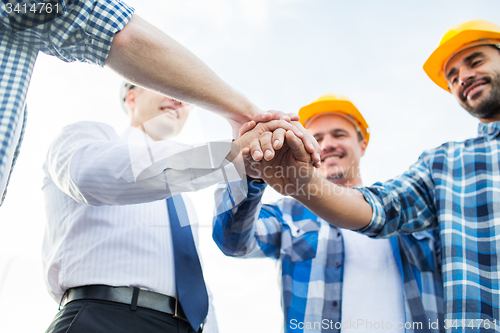 Image of close up of builders in hardhats with hands on top