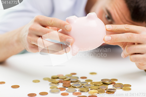 Image of close up of man pouring coins from piggy bank