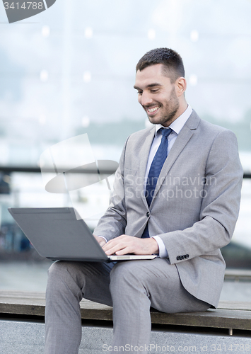 Image of smiling businessman working with laptop outdoors