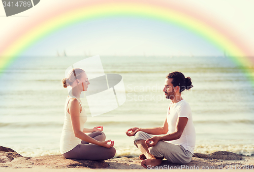 Image of happy couple meditating in lotus pose on beach