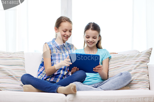 Image of happy girls with tablet pc sitting on sofa at home