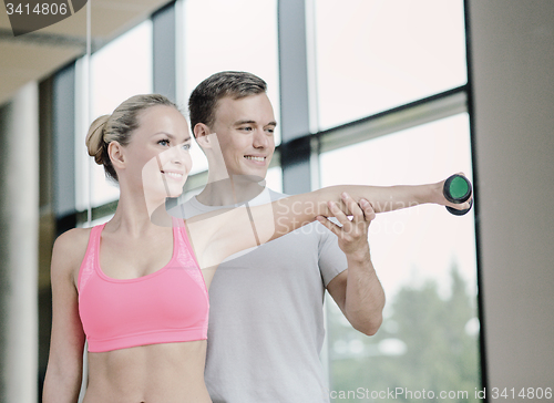 Image of smiling young woman with personal trainer in gym