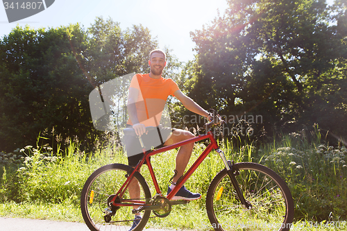 Image of happy young man riding bicycle outdoors