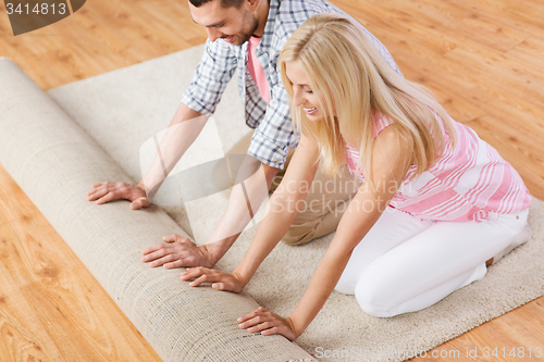 Image of happy couple unrolling carpet or rug at home
