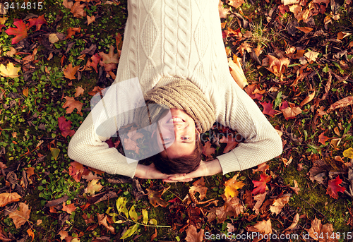 Image of smiling young man lying on ground in autumn park