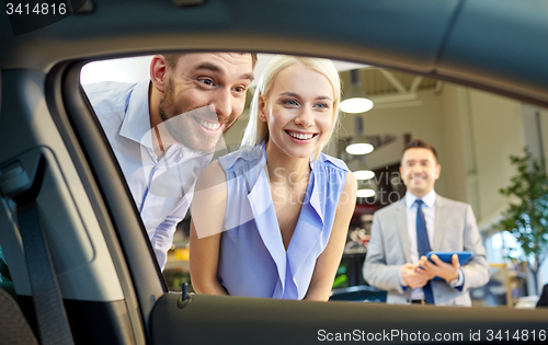 Image of happy couple with car dealer in auto show or salon