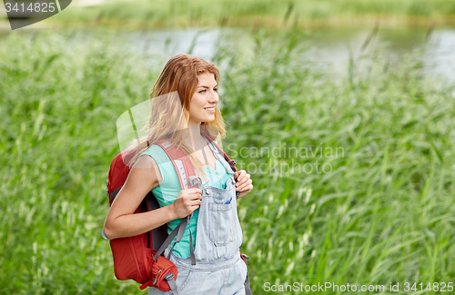 Image of smiling young woman with backpack hiking in woods