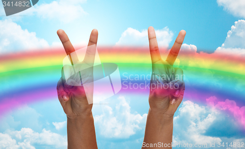 Image of hands showing peace sign over rainbow in sky