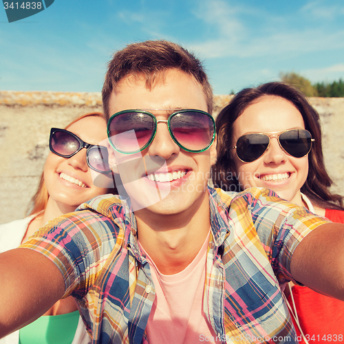 Image of group of smiling friends taking selfie outdoors