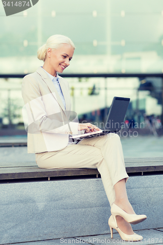 Image of smiling businesswoman working with laptop outdoors