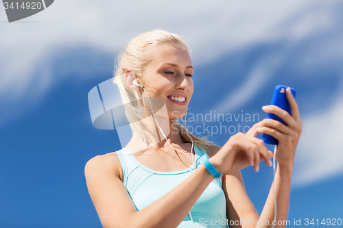 Image of happy woman with smartphone and earphones outdoors